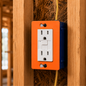 Orange electrical outlet cover with a white wall socket on a wooden wall.