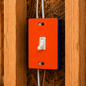 Orange light switch panel with white switch on a wooden wall.